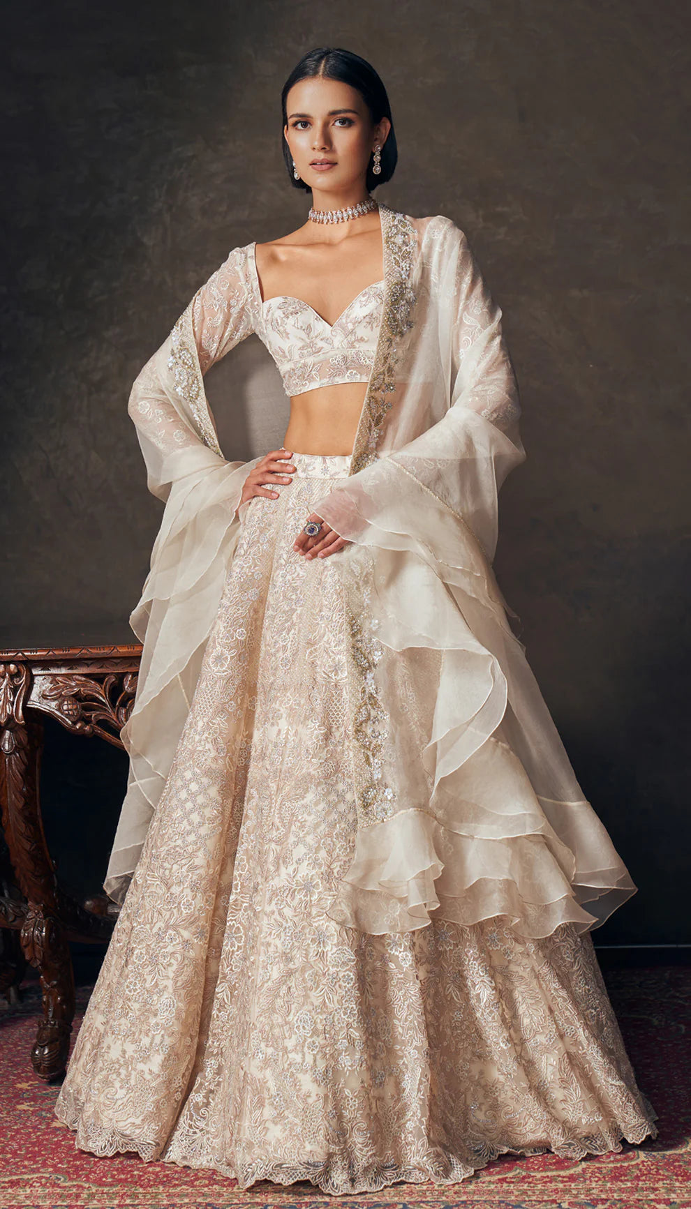 Woman wearing an ivory traditional embroidered lehenga by designers Shyamal and Bhumika with a dark background