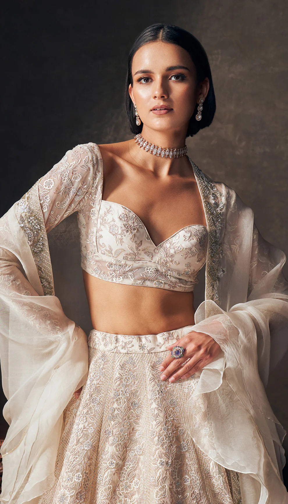 Woman wearing an ivory traditional embroidered lehenga by designers Shyamal and Bhumika with a dark background