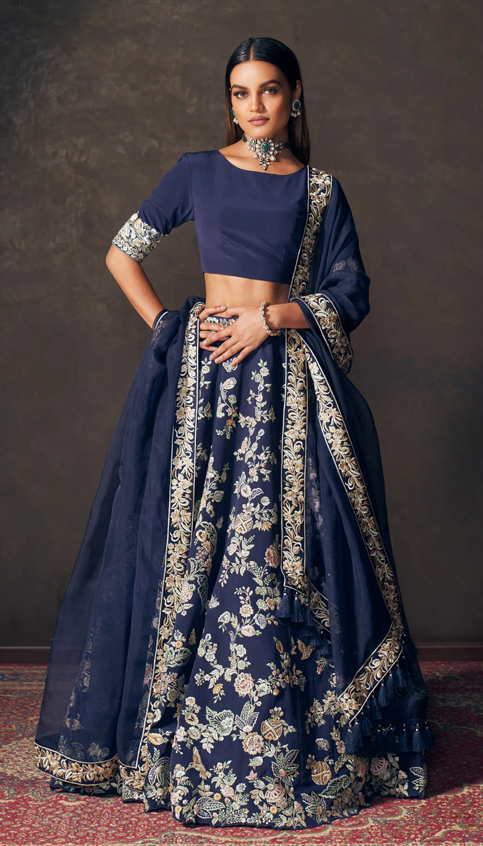 Woman wearing a traditional navy blue lehenga with floral patterns by designers Shyamal and Bhumika on a dark background
