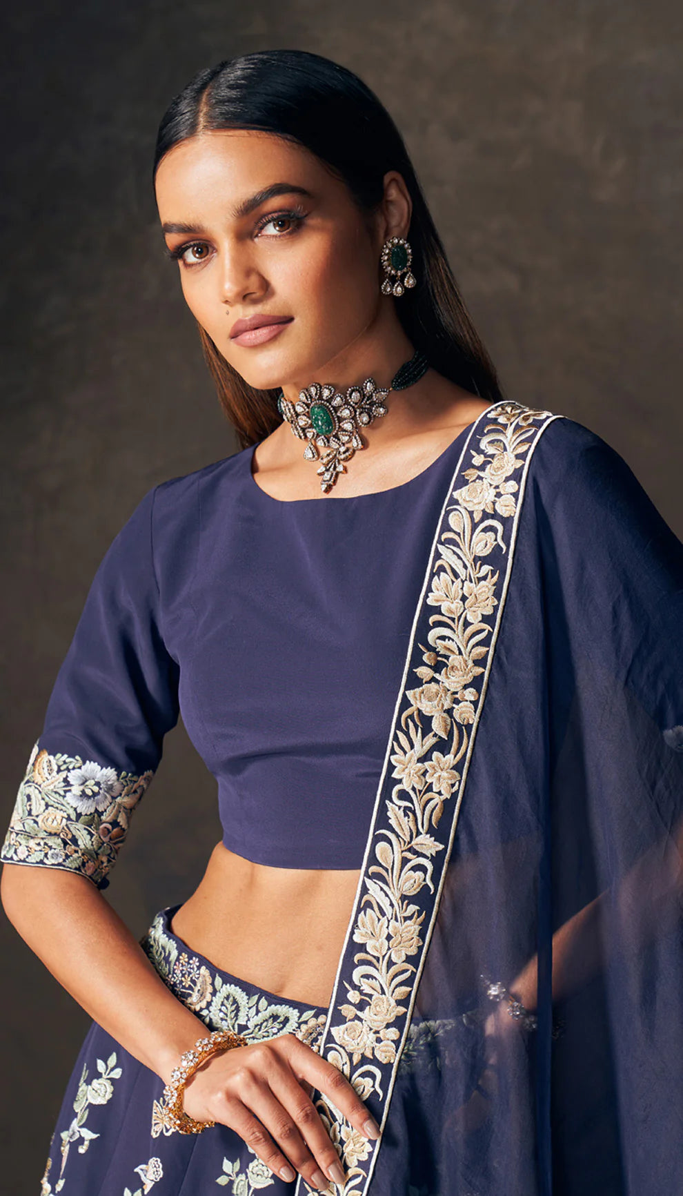 Woman wearing a traditional navy blue lehenga with floral patterns by designers Shyamal and Bhumika on a dark background