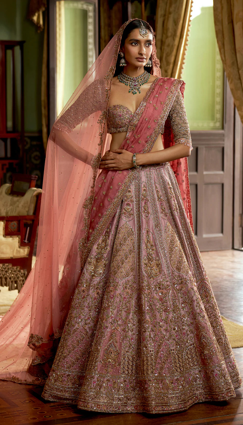 Woman in traditional pink and gold embroidered lehenga with a matching dupatta by designers Shyamal and Bhumika in an indoor setting.