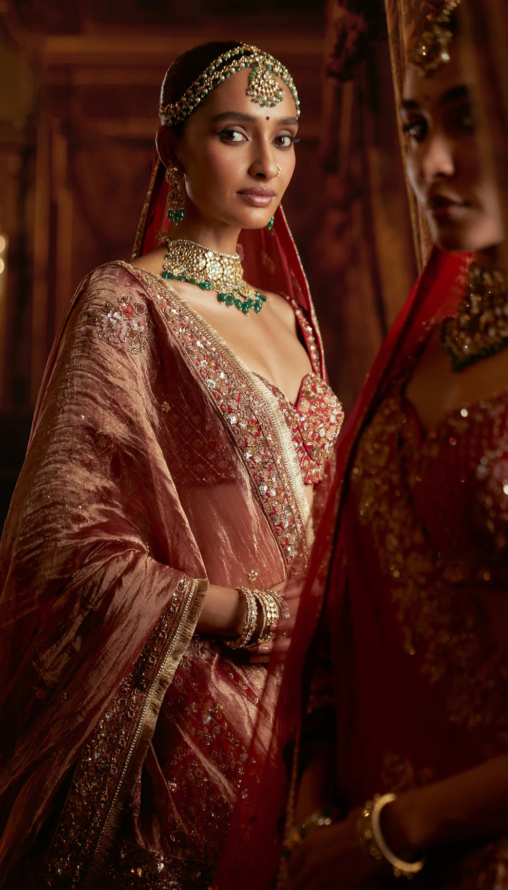 Woman in a red traditional embroidered bridal lehenga by designers Shyamal and Bhumika with a rich background