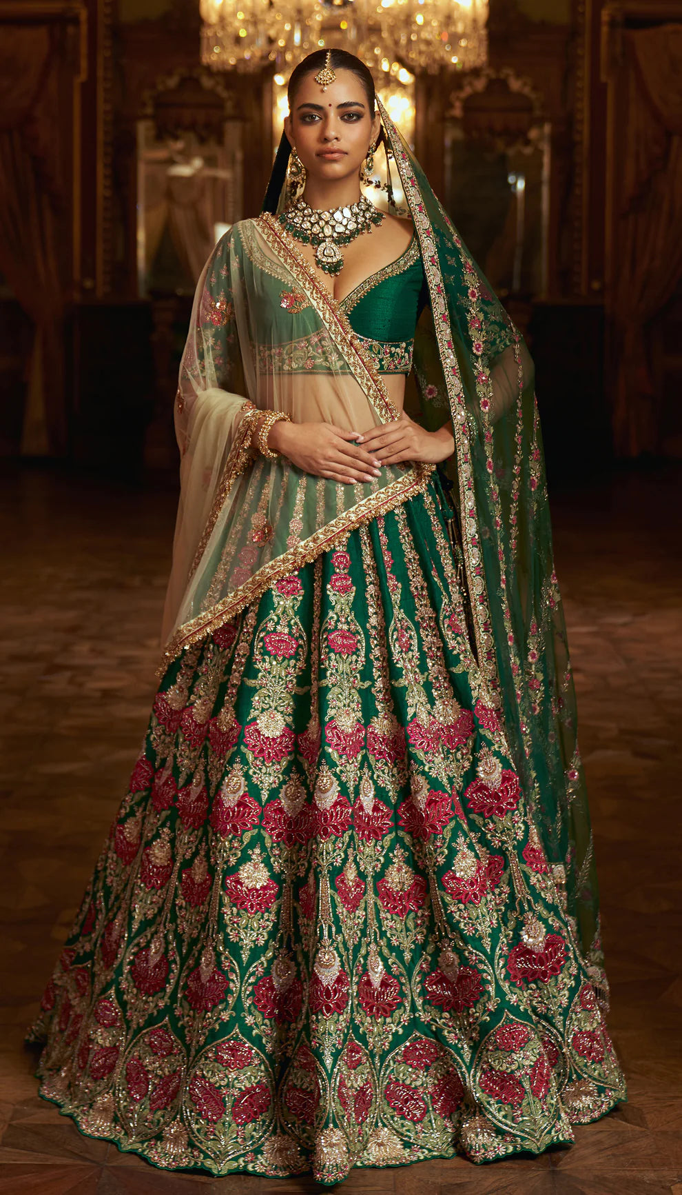 Woman in a traditional green and pink embroidered lehenga by designers Shyamal and Bhumika with jewelry in an indoor setting.