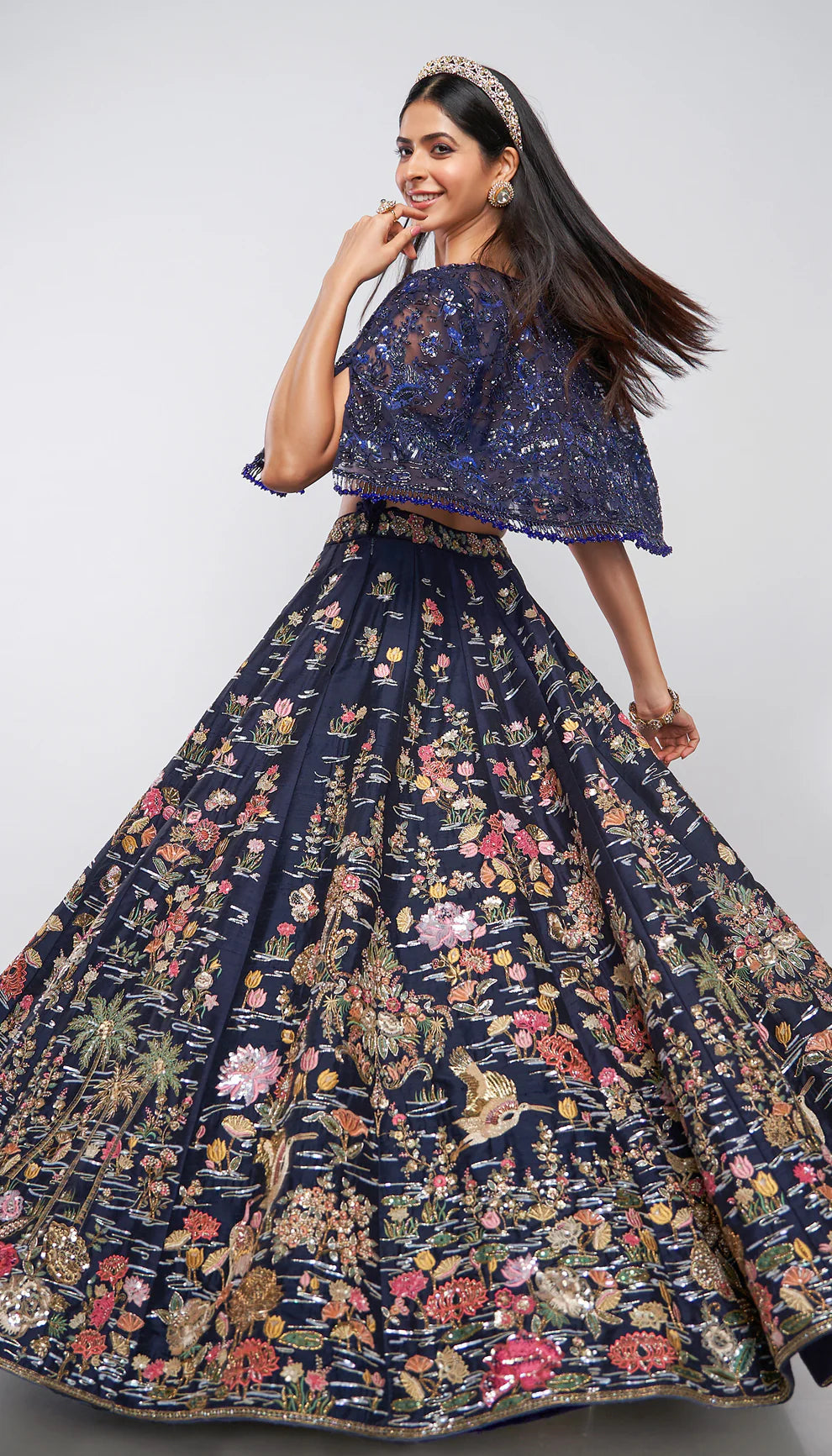Model wearing a dark blue floral lehenga on a runway with a blurred floral background for designers Shyamal and Bhumika