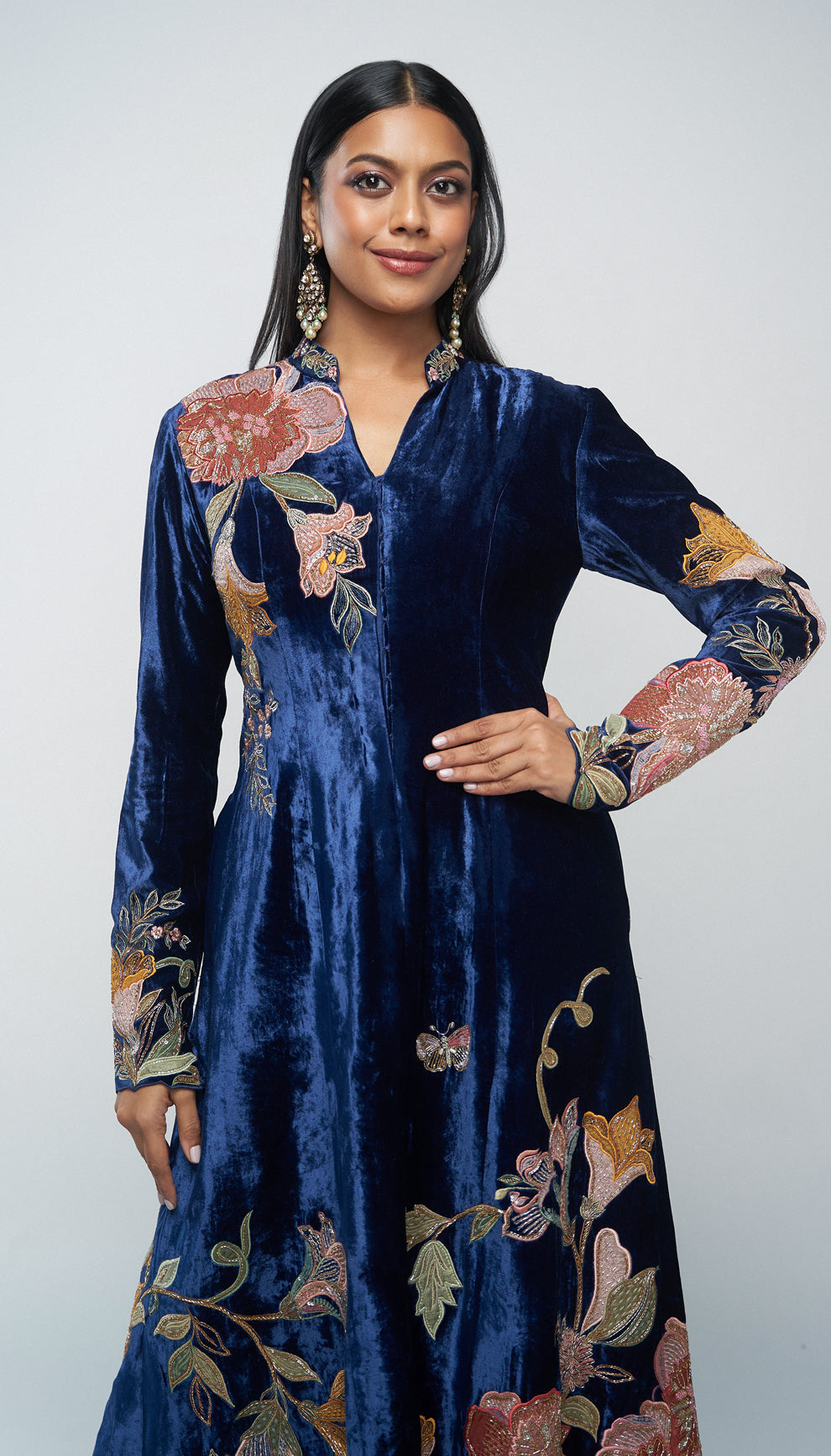 Woman in a blue velvet jacket with floral embroidery walking on a runway with a floral background by designers Shyamal and Bhumika