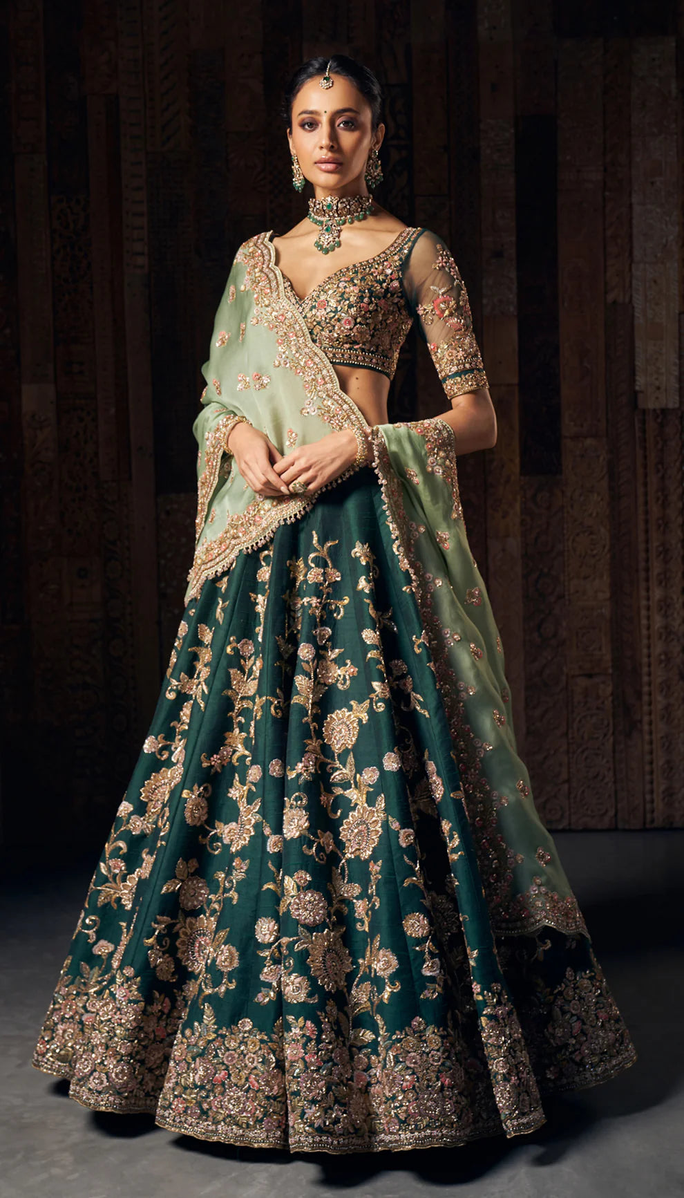 Woman wearing a traditional green and gold lehenga by designers Shyamal and Bhumika with a dark background