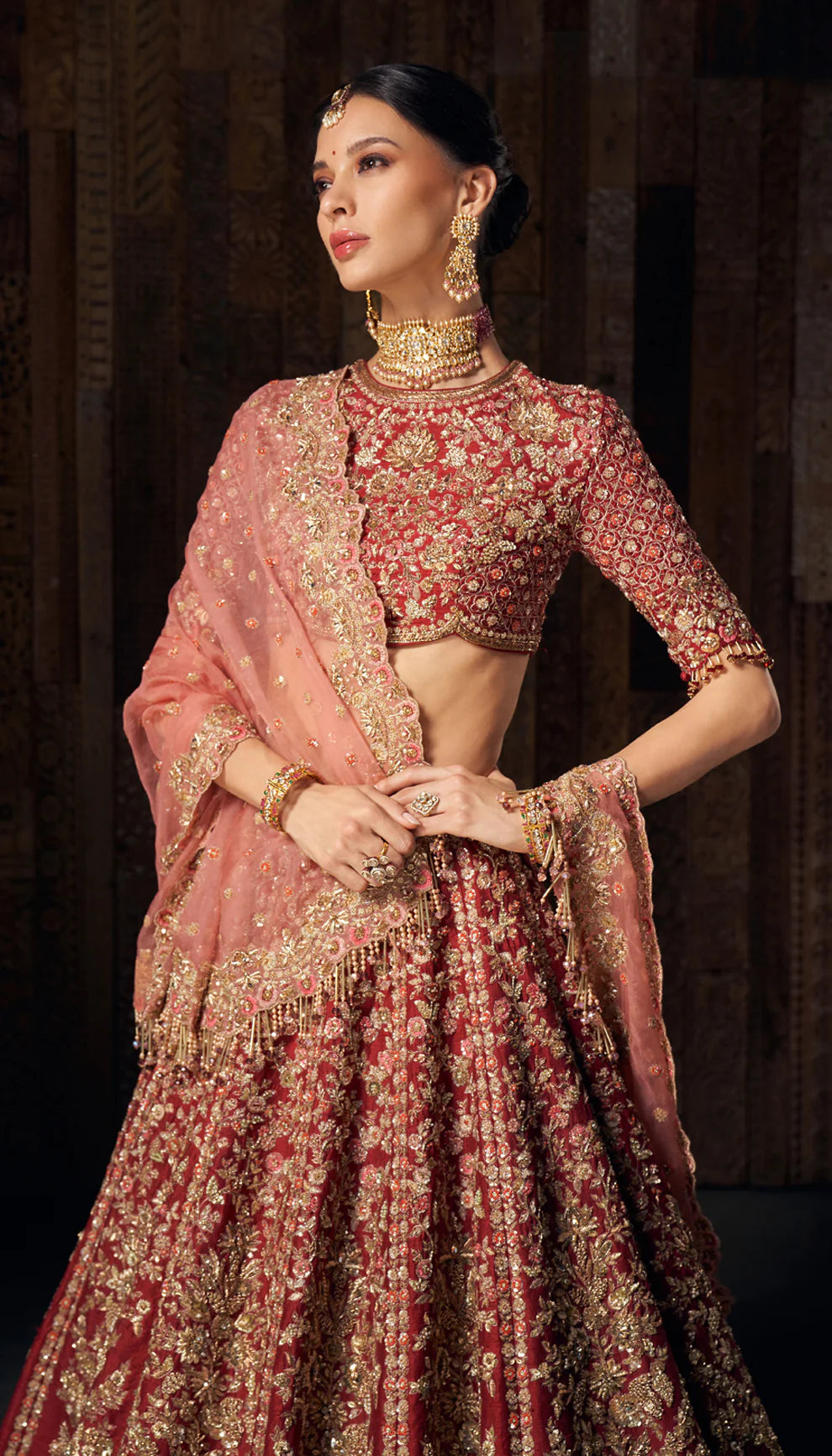Woman in deep red gold embroidered bridal lehenga by designers Shyamal and Bhumika, against a dark backdrop