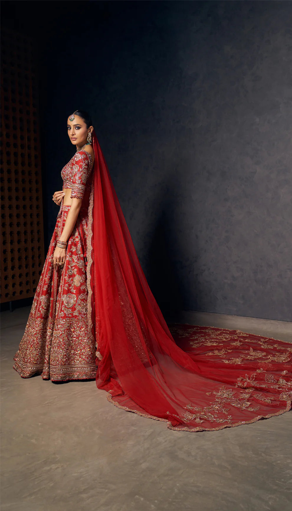 Woman wearing a red and gold embroidered bridal lehenga by designers Shyamal and Bhumika against a dark background
