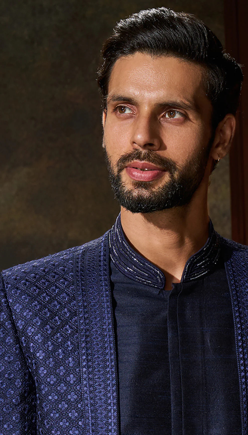 Man wearing a blue embroidered jacket by designers Shyamal and Bhumika against a dark background