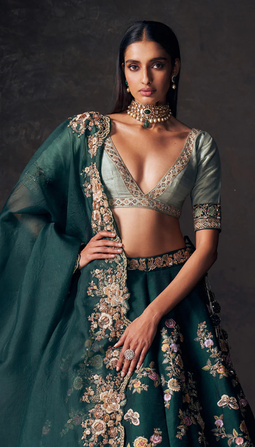 Woman wearing a traditional forest green lehenga with a floral design by designers Shyamal and Bhumika on a dark background