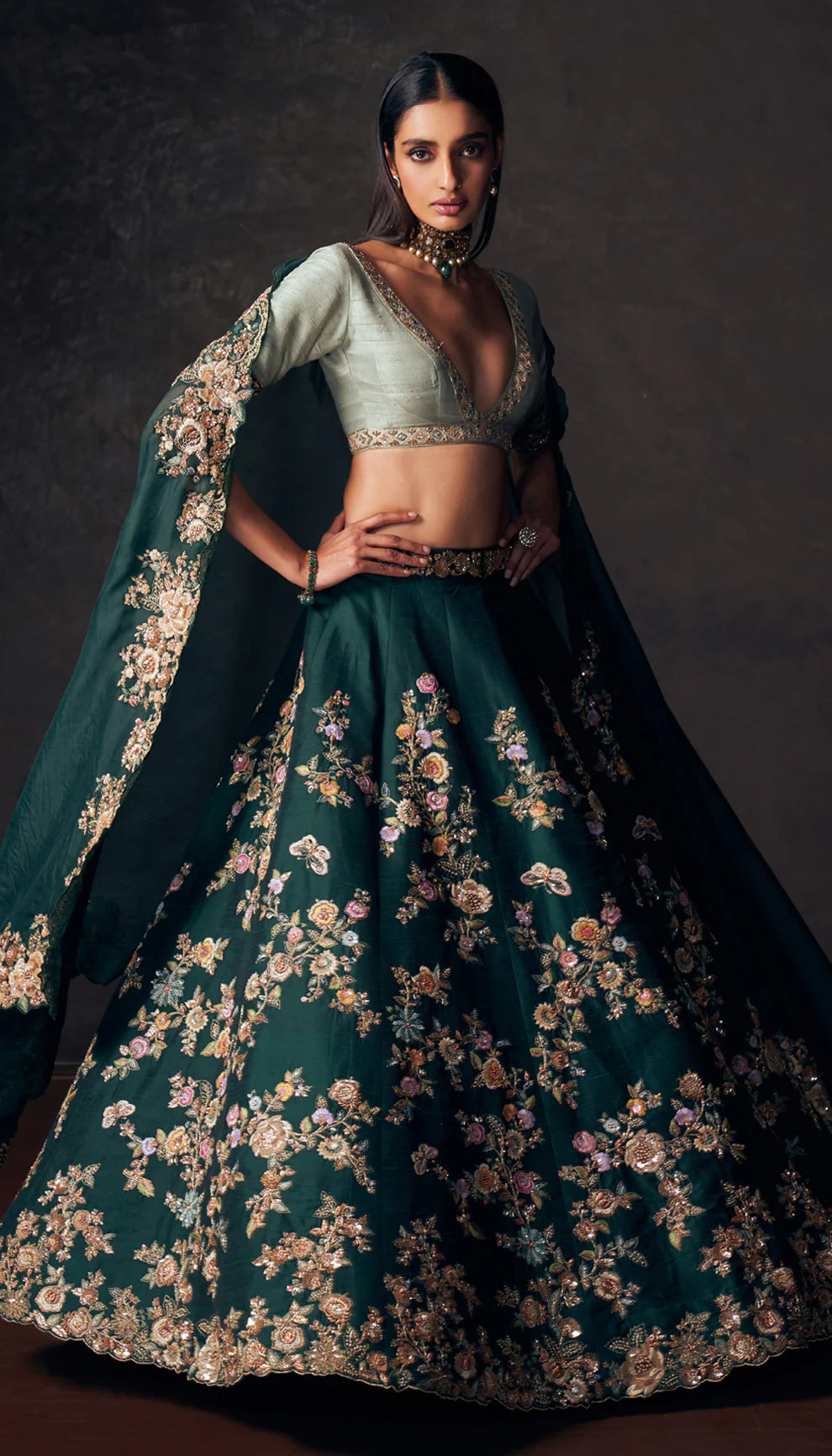 Woman wearing a traditional forest green lehenga with a floral design by designers Shyamal and Bhumika on a dark background