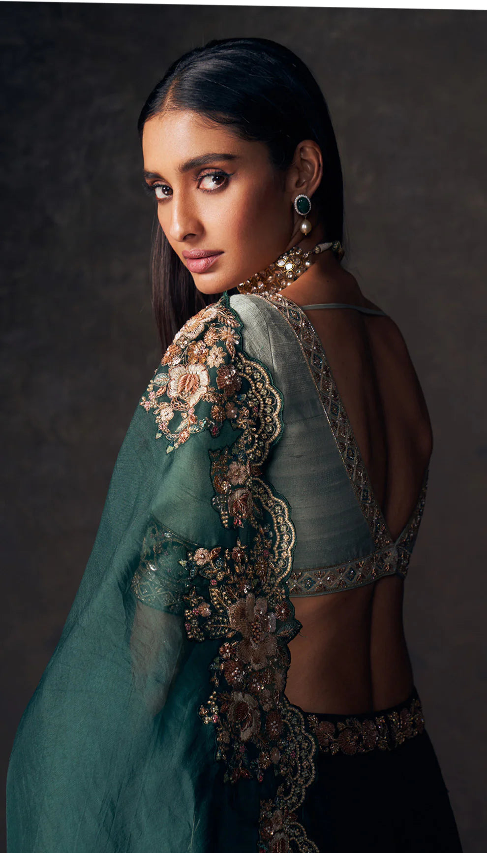 Woman wearing a traditional forest green lehenga with a floral design by designers Shyamal and Bhumika on a dark background