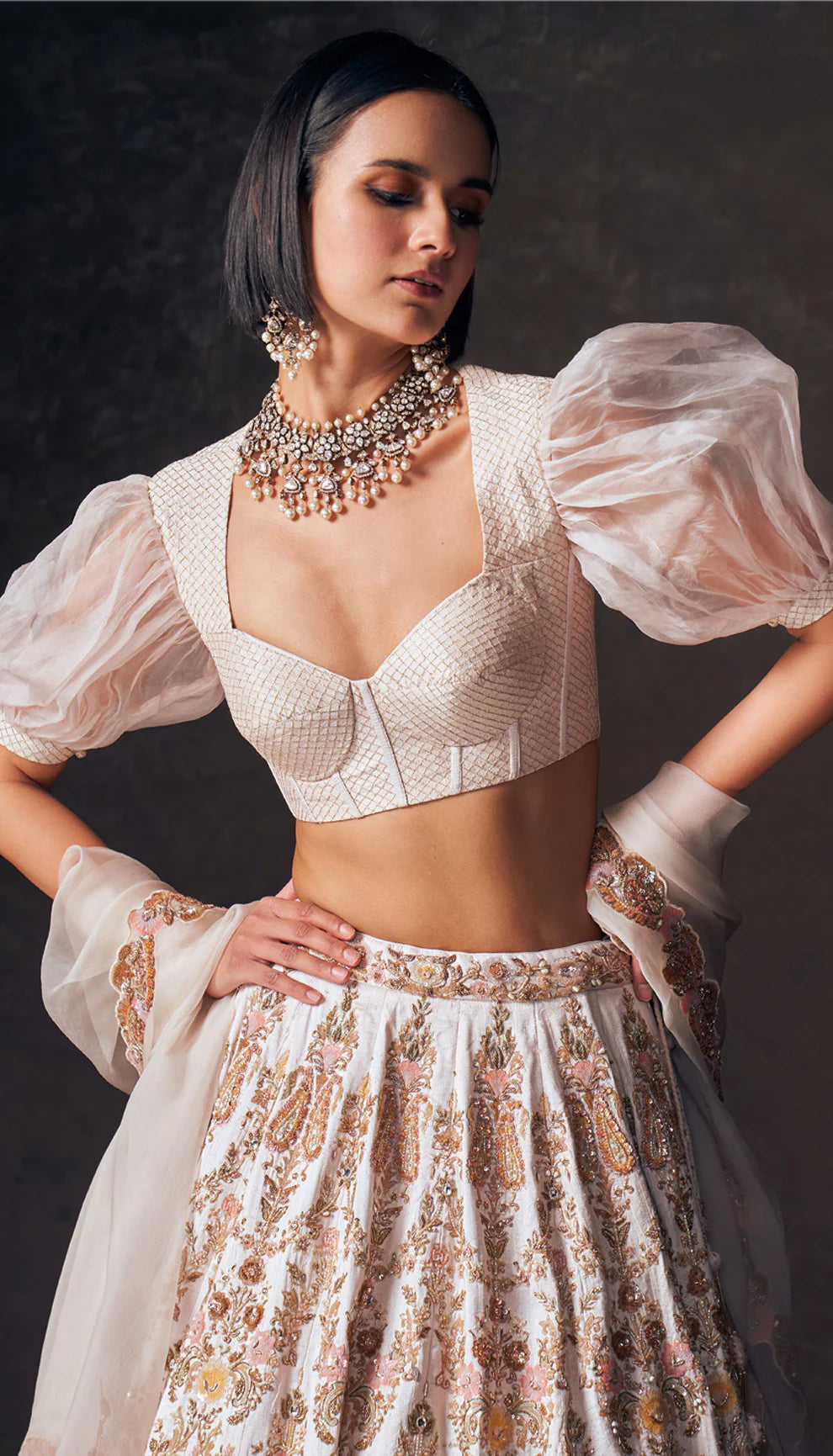 Woman wearing an ivory traditional lehenga with a white blouse and patterned skirt by designers Shyamal and Bhumika against a dark background