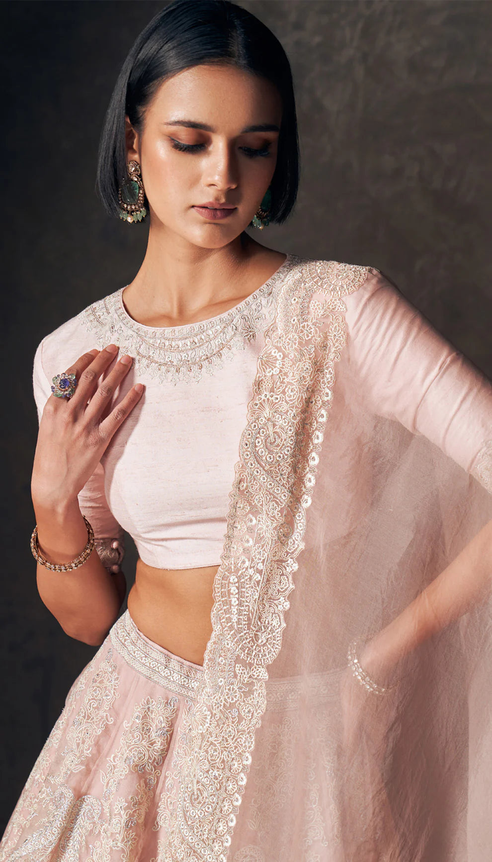 Woman wearing a traditional pink lehenga with a matching blouse by designers Shyamal and Bhumika against a dark background