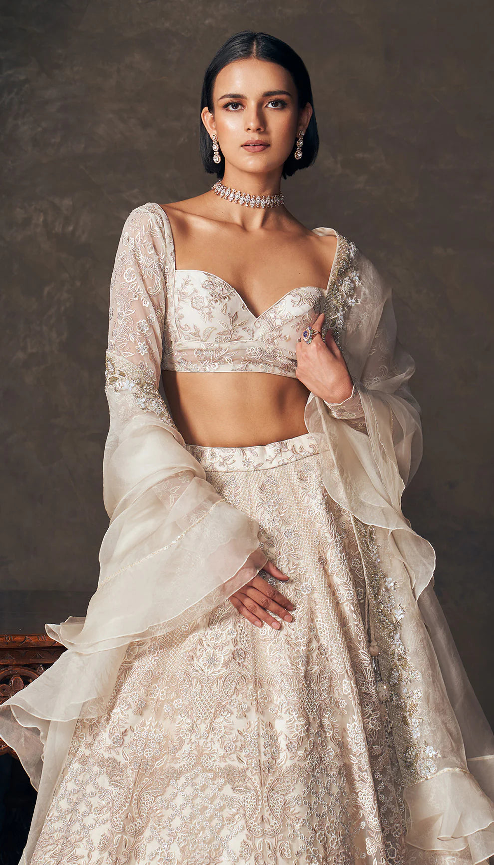 Woman wearing an ivory traditional embroidered lehenga by designers Shyamal and Bhumika with a dark background